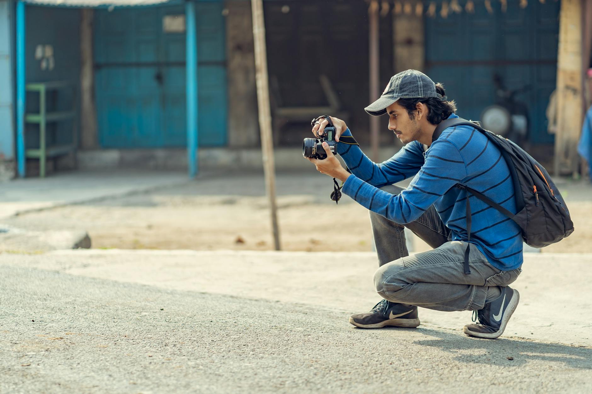 Młody fotograf kuca w mieście, robiąc zdjęcie aparatem DSLR